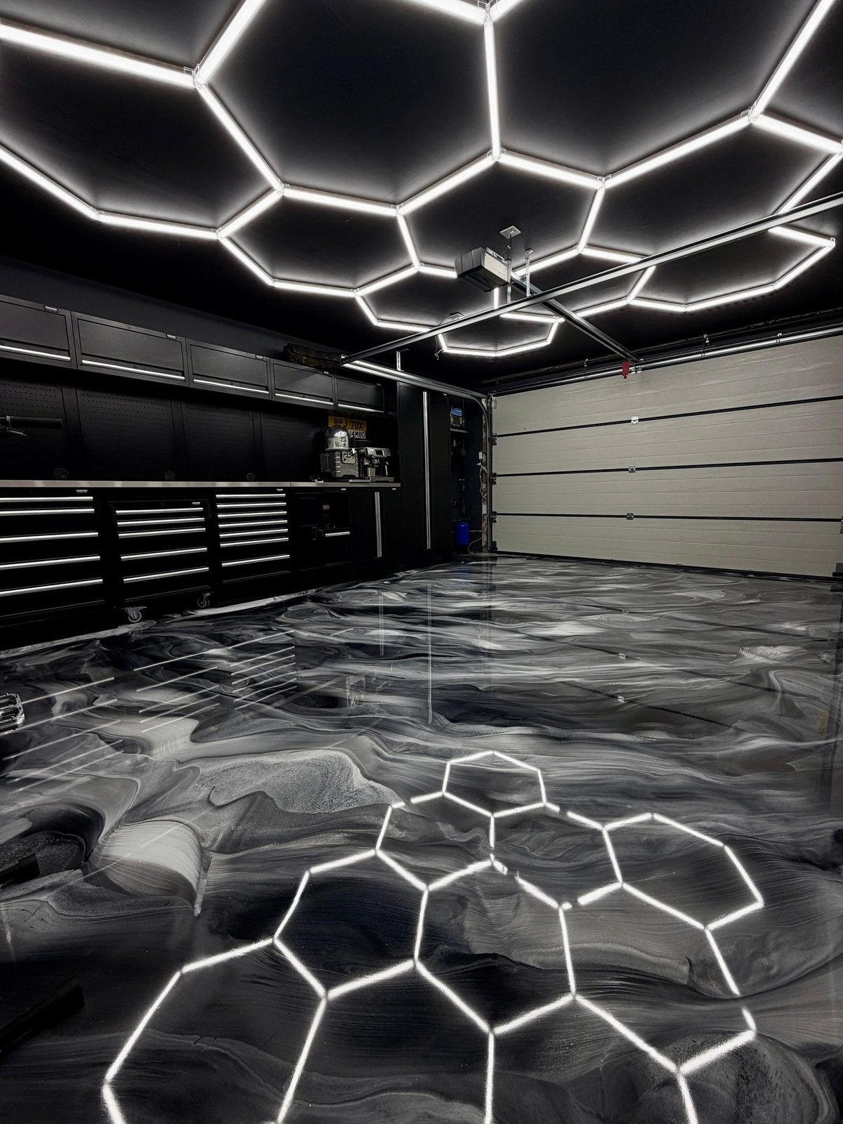 Modern garage interior with hexagonal neon lighting on ceiling and floor, black tool drawers, and reflective concrete floor
